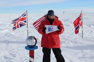 Jamie Hensel (S'03) stands holding the Williams-Mystic burgee at the ceremonial South Pole.