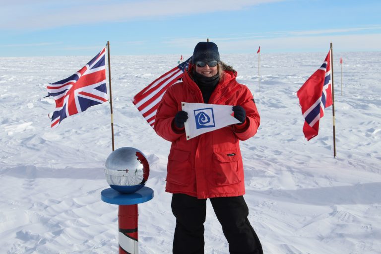 Jamie Hensel (S'03) stands holding the Williams-Mystic burgee at the ceremonial South Pole.