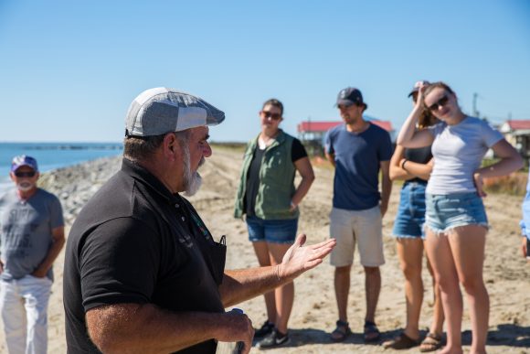 A man speaks to students on a beach.