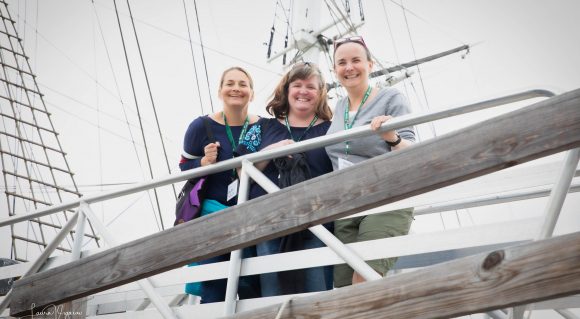 image shows three women smiling aboard a historic tall ship