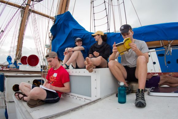 Four students sitting on a boat deck, two are studying.